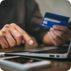 Hands type a credit card number on a laptop.